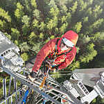 Telecommunication manual high worker engineer installing new 3g 4g LTE antenna on tall mobile base station (communication tower) in the middle of european forest, high angle of view. Working at height. Telecommunication masts and towers are typically tall structures designed to support antennas for telecommunications and broadcasting. Drone point of view.