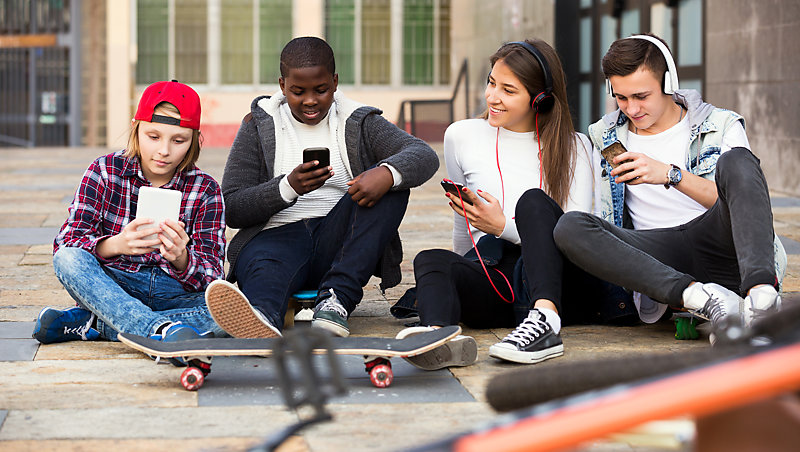 Teenagers sitting on the ground with eyes on their mobile phones.