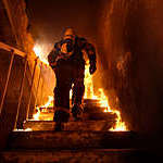Back view of a firefighter going up the stairs of a burning building. 