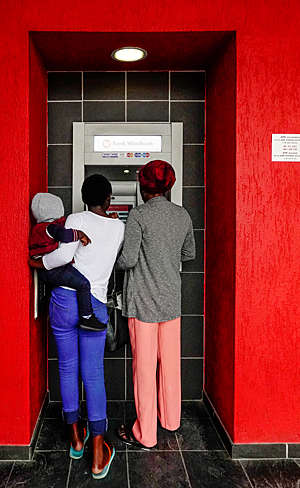 Rear view of two women, one carrying a child, withdrawing money from a cash machine in Namibia.
