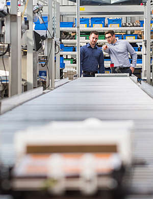 Two men talking at a conveyor belt on the factory shop floor.