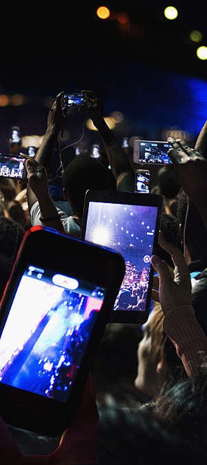 Close view of a crowd of people recording video with their cell phones at night.