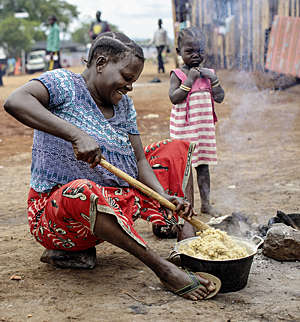 Refugee women from the Congo cooks food sitting on the ground at the Kyangwali Refugee Settlement in Uganda.