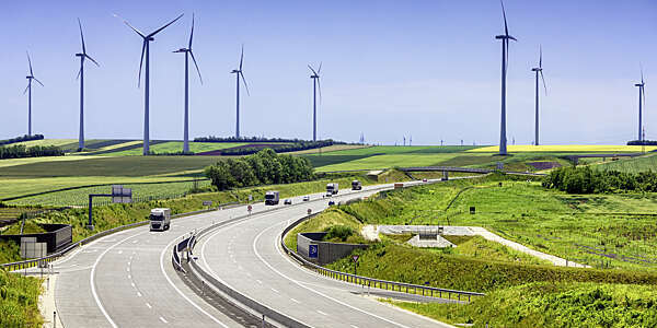 Highway running through green fields with wind turbines on the horizon.