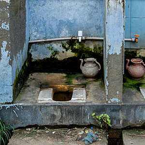 Two dilapidated open-air squatting toilets with scaling blue-painted walls.