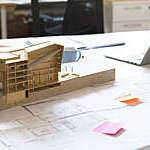 Desk with architectural model of a building, and out-of-focus coffee cup and laptop.