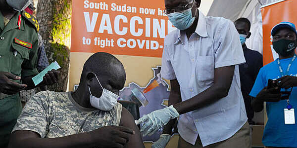 Military general, seated, receives the COVID-19 vaccine from a healthcare professional at the Juba military hospital in South Sudan.