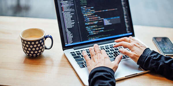 Close-up of woman's hands typing on a laptop with a cup of coffee by her side.