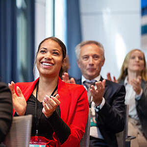 Business people applauding during launch event in convention center. Male and female business professionals attending seminar in auditorium clapping hands.
