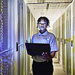 Medium shot portrait of female IT professional holding laptop while standing in row of servers in data center