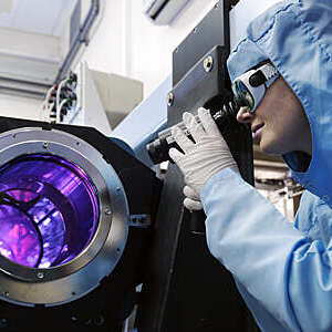 Female scientist in protective clothing and goggles uses a purple beam laser equipment.